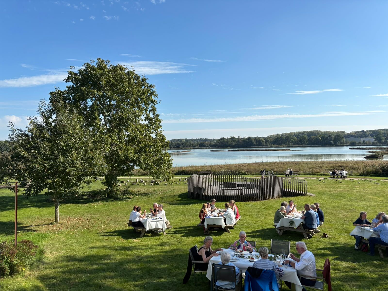 Gezelschappen aan gedekte tafels op het gazon, met het meer van Het Vinne op de achtergrond